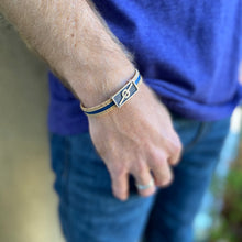 Load image into Gallery viewer, Man with hand in  his jeans pocket wearing a Stoke Saver Onewheel™ bracelet in rustic cork with navy blue inlay strap and stainless steel clasp
