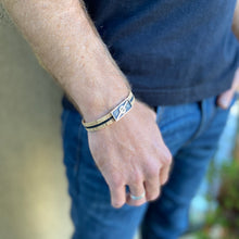Load image into Gallery viewer, Man with hand in  his jeans pocket wearing a Stoke Saver Onewheel™ bracelet in rustic cork with black inlay strap and stainless steel clasp
